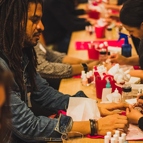 Man with dreadlocks getting a manicure at a busy event table