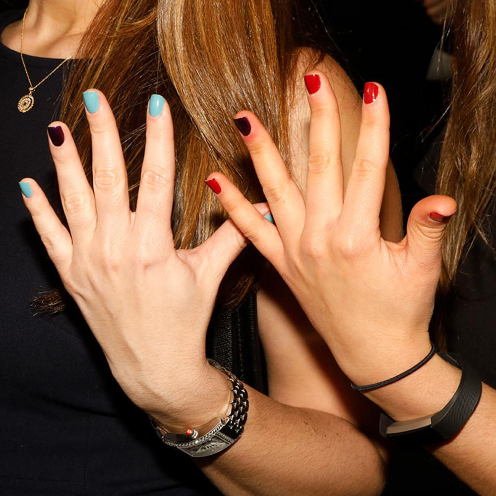 Two hands showing teal and burgundy manicures against a dark event background