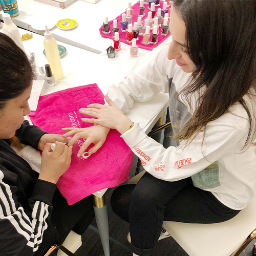 Technician painting nails at a station full of colorful polish bottles