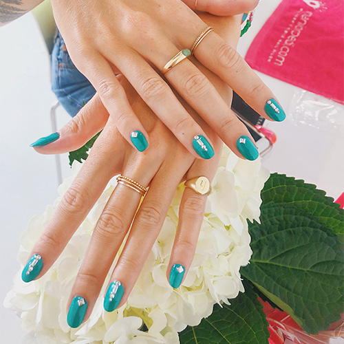 Teal manicure with rhinestone nail art held over white hydrangeas