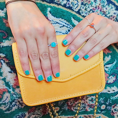 Teal manicure resting on a yellow crossbody bag