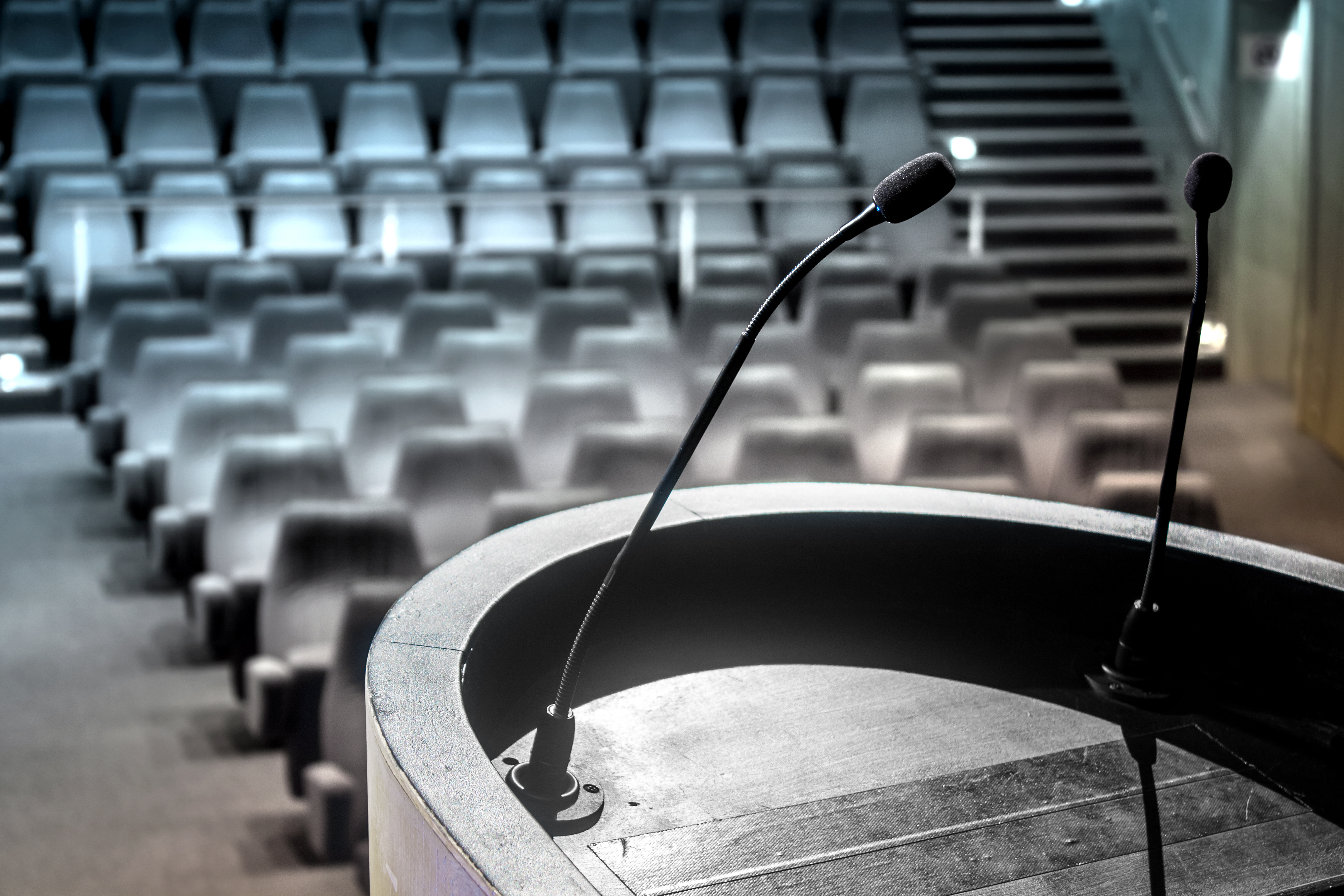 A lecture-hall podium with microphones in front of rows of empty auditorium seats