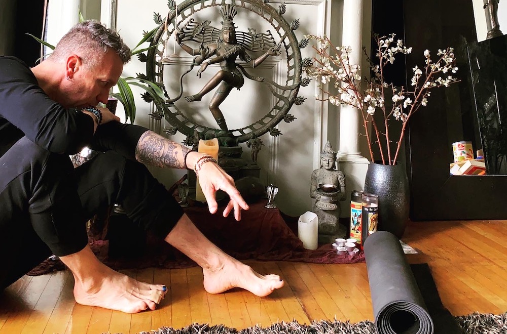 Mark Morford seated on the floor beside his altar with a Nataraja statue, candles and a Buddha figurine