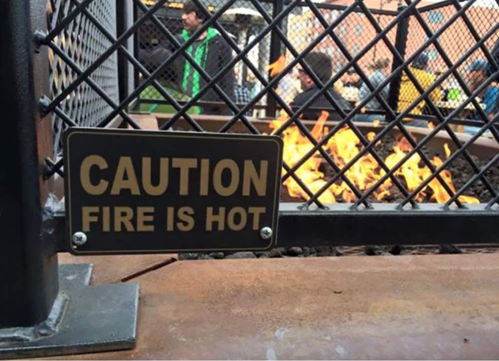 A 'Caution: Fire Is Hot' sign in front of an open fire