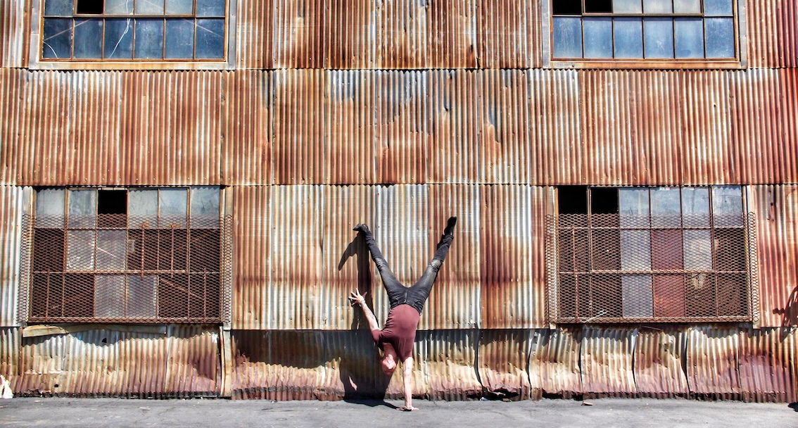 Mark Morford in a handstand against a rusted corrugated warehouse wall