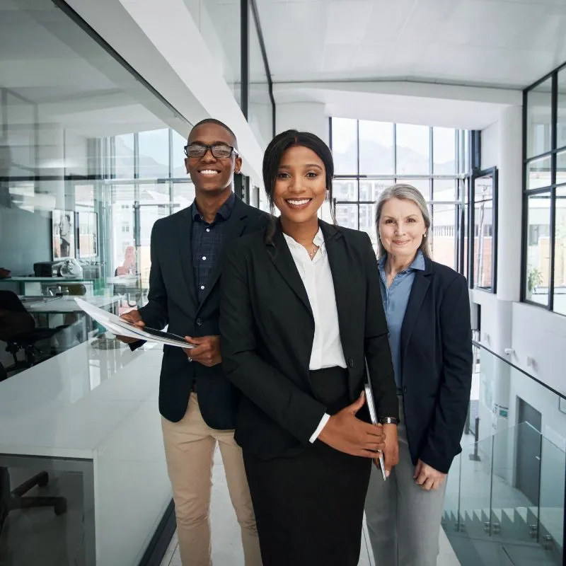 Three business professionals smiling in a bright modern office hallway