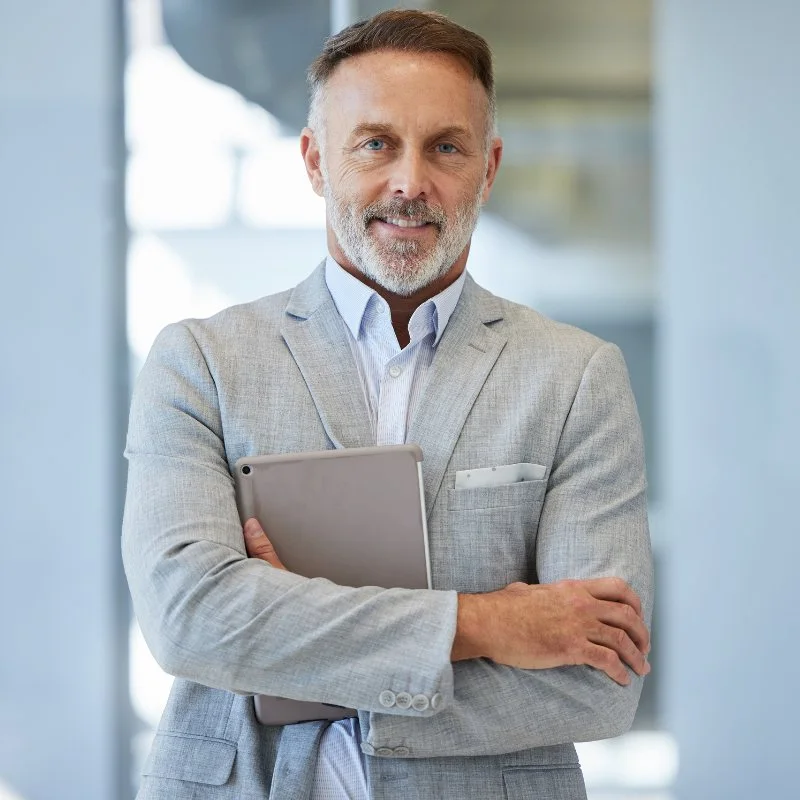 Executive in a light grey blazer holding a tablet, arms crossed