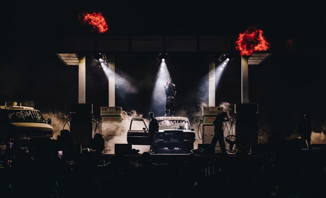 Custom gas-station stage set with a performer atop a car and fire bursts