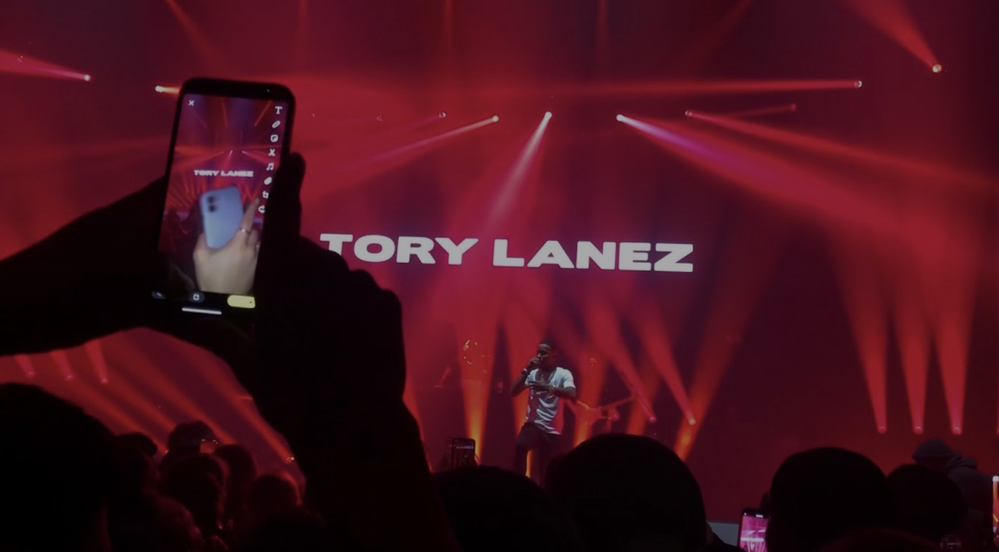 Full-house crowd under red wash with Tory Lanez on the backdrop screen