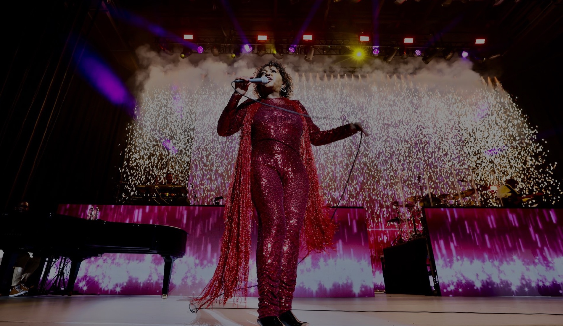 Performer in a red sequin jumpsuit on stage with pyrotechnic confetti effects and piano staging