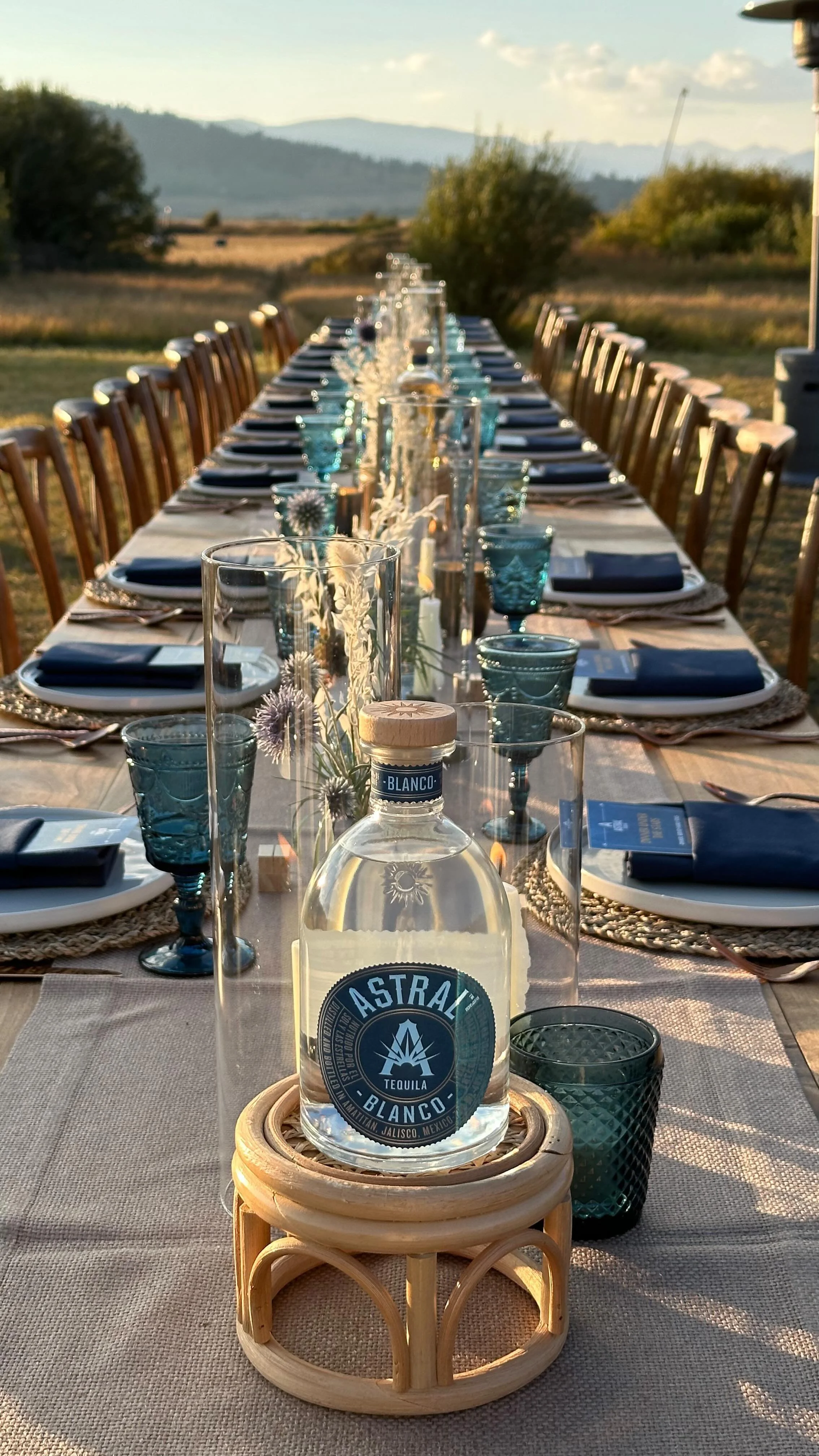 Long tablescape with Astral Tequila Blanco centerpiece and teal glassware at golden hour.