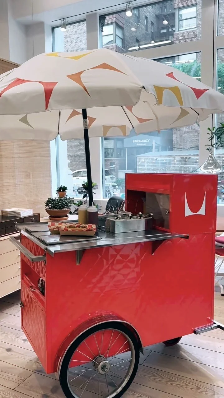Red branded food cart with patterned umbrella inside a Gramercy retail space, New York.