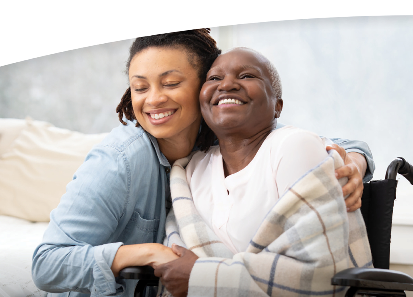 A young woman embracing an elderly woman in a wheelchair, both smiling