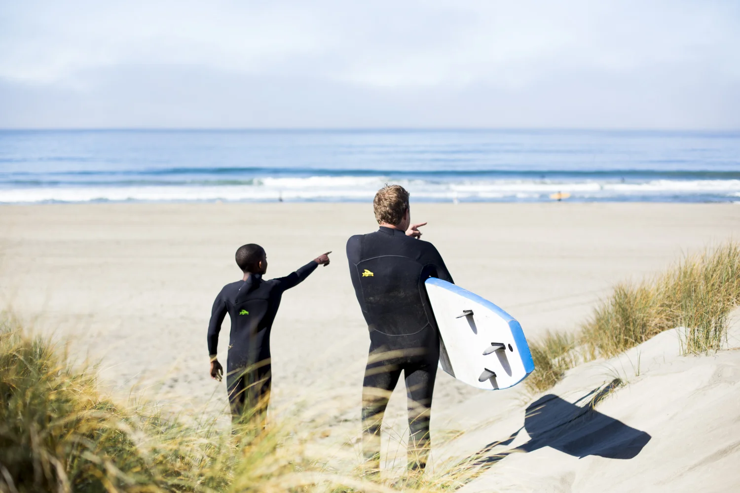 An instructor and a child in wetsuits standing in the dunes, pointing out at the ocean