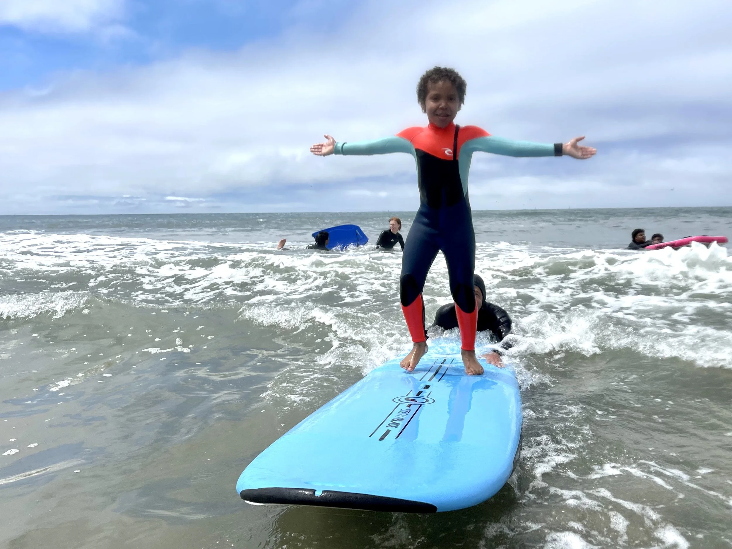 A young child standing on a surfboard riding a wave with arms outstretched