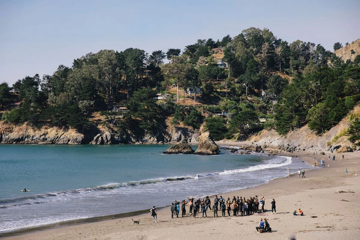A cove beach with wooded bluffs and a MeWater camp group gathered at the shoreline