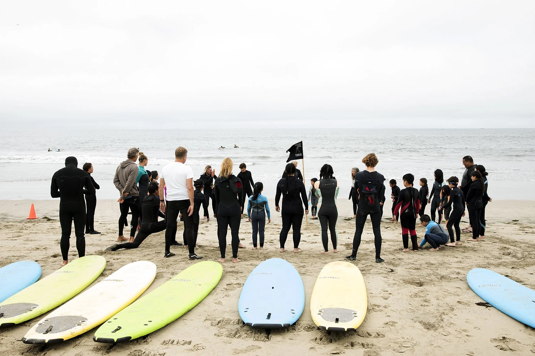 A large group of camp participants and instructors gathered on the beach with surfboards laid out