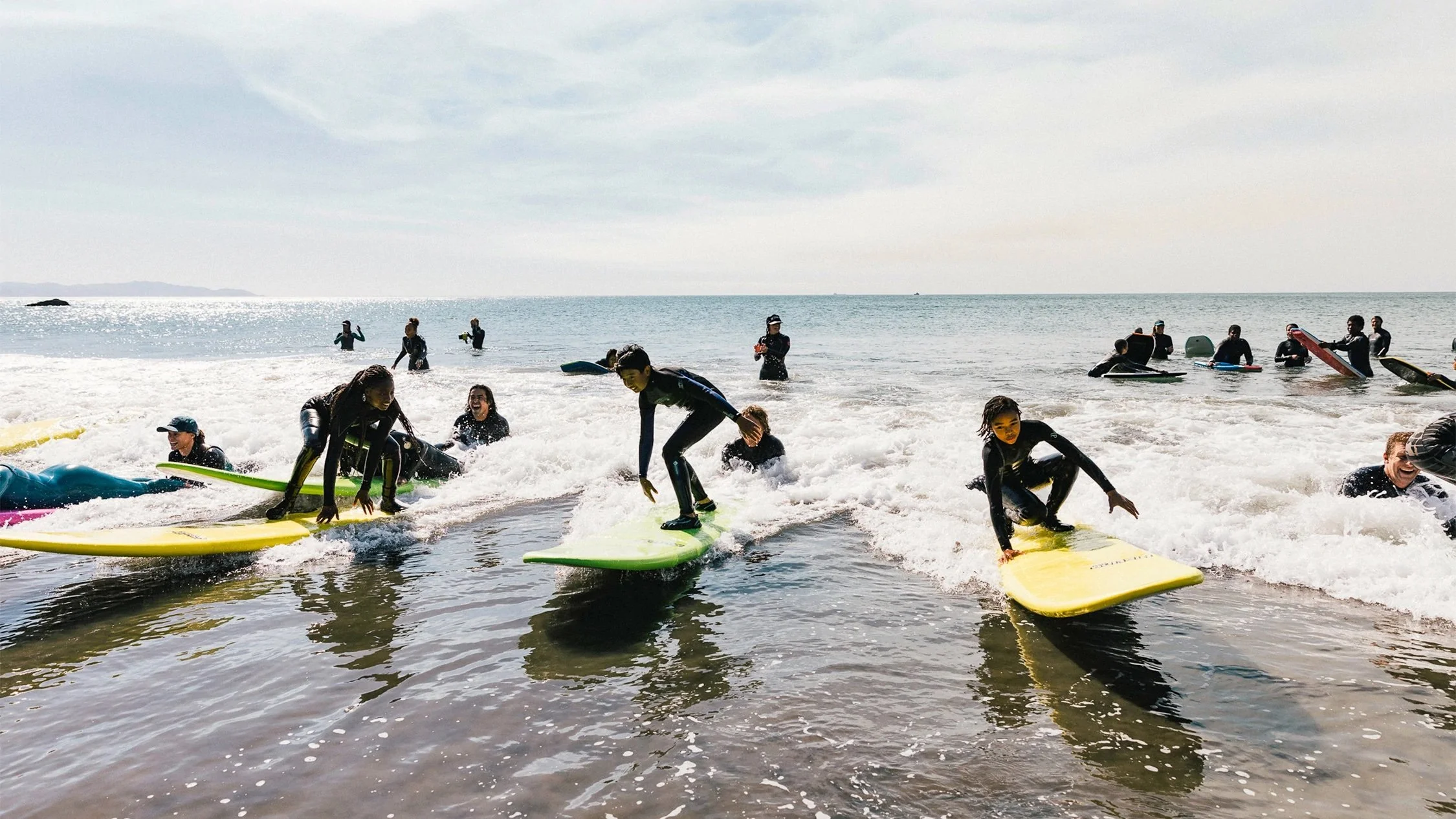 Several youth riding small waves on surfboards during a group surf lesson