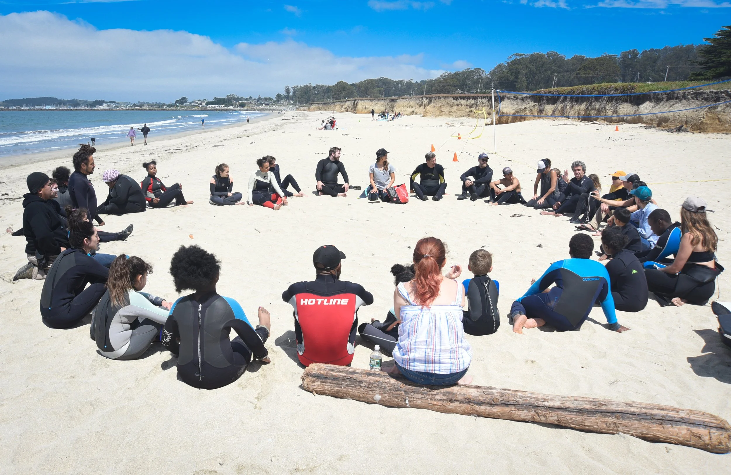 A large group of camp participants seated in a circle on the beach for a discussion