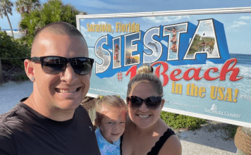 Family of three taking a selfie at the Siesta Beach sign in Sarasota