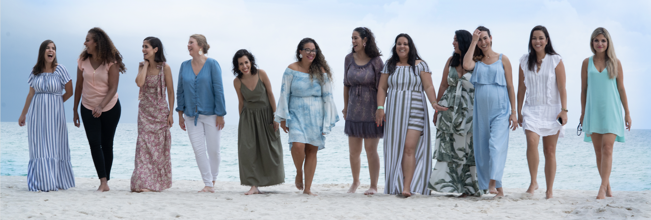 About twelve Miami Mom Collective women walking together on the beach in pastel dresses