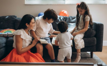 Woman in an orange skirt with three young children looking at a book on a couch