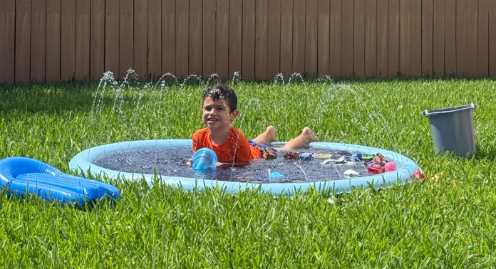 Young boy in an orange shirt playing in a backyard splash pad on a sunny day