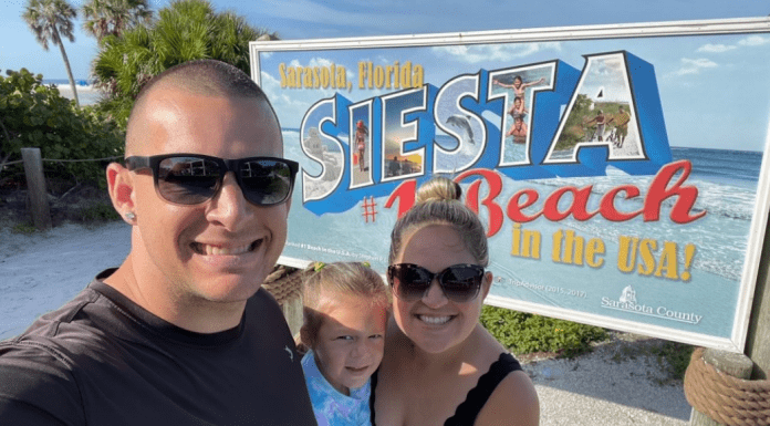 Family of three taking a selfie in front of the Siesta Beach #1 Beach in the USA sign in Sarasota, Florida