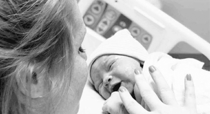 Black-and-white photo of a woman holding and gazing at her newborn baby in a hospital