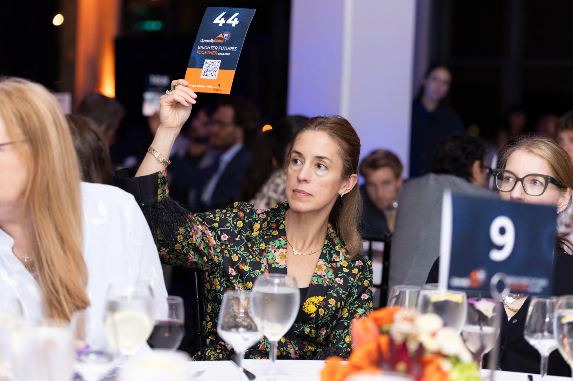 A guest in a floral dress raising paddle number 44 during a fundraising gala paddle raise