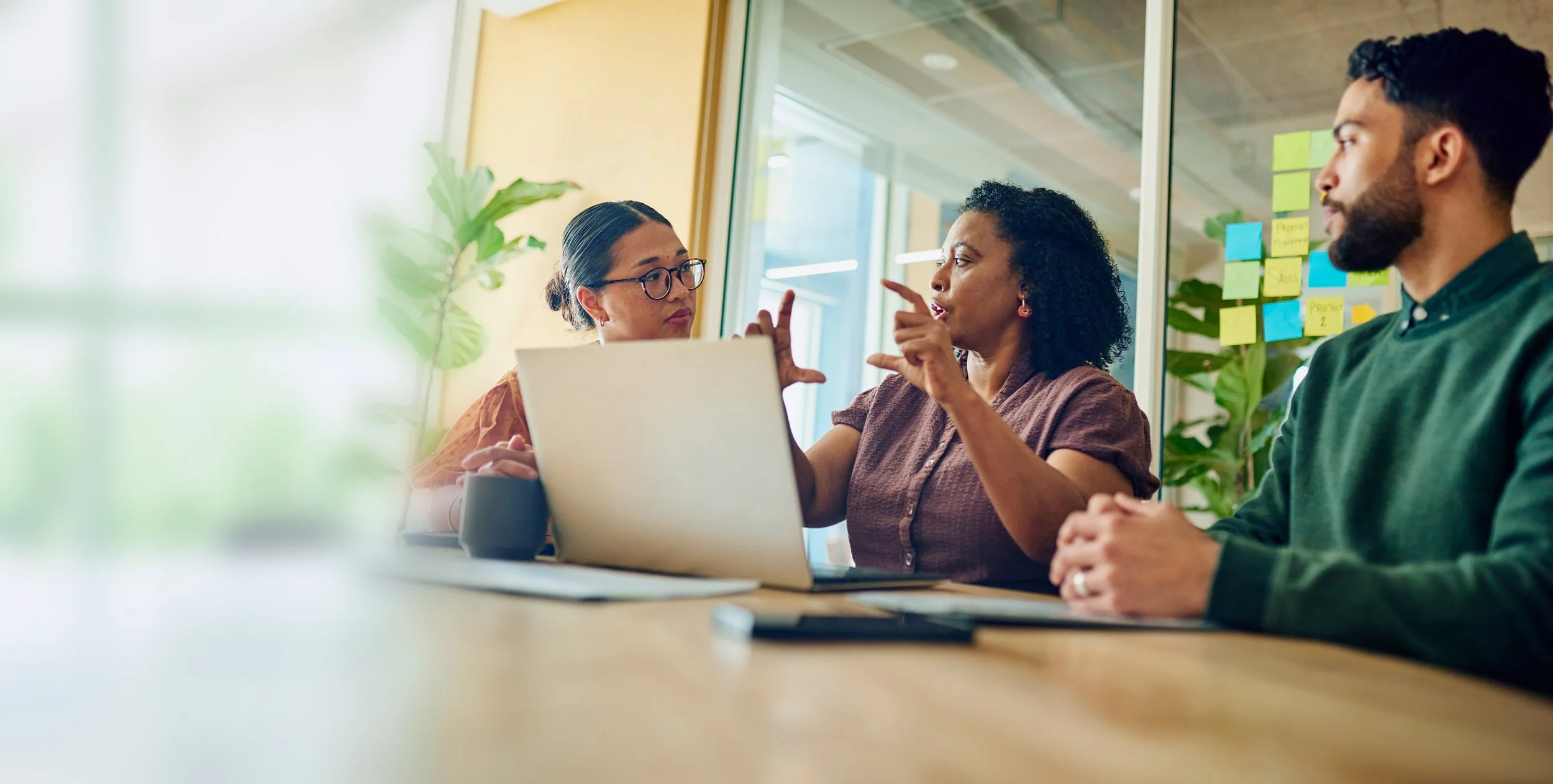 Three professionals collaborating around a laptop in a bright office meeting room
