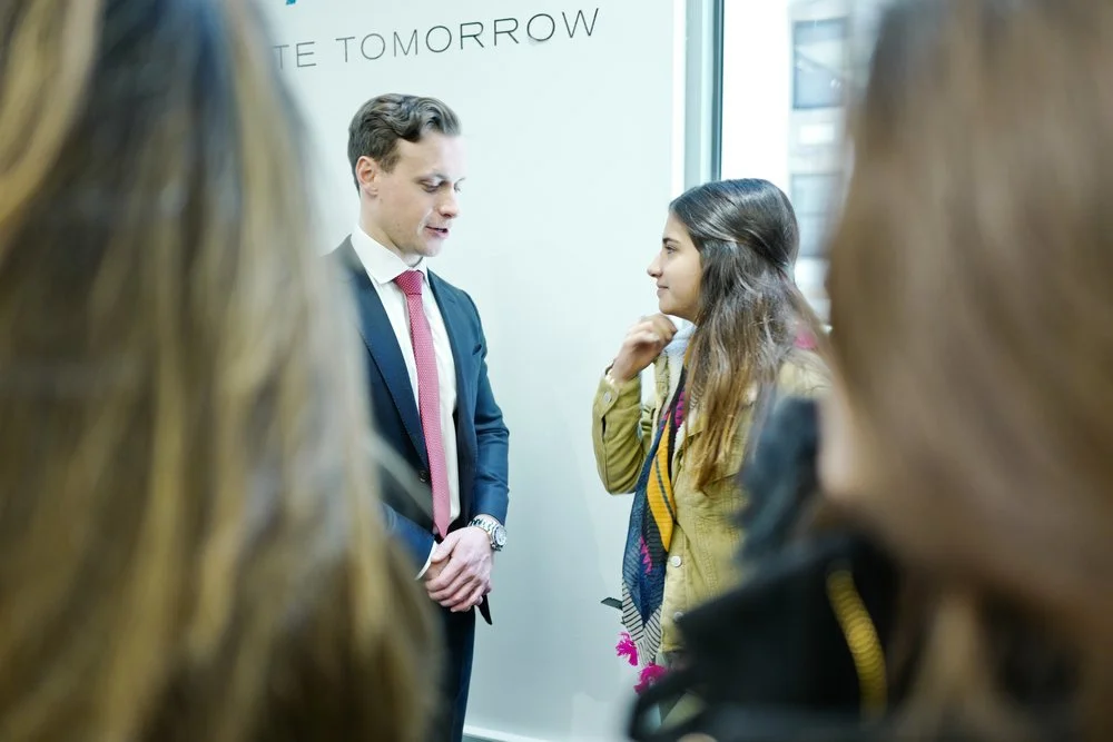 A partner in a dark suit talking with a student in front of a Create Tomorrow banner