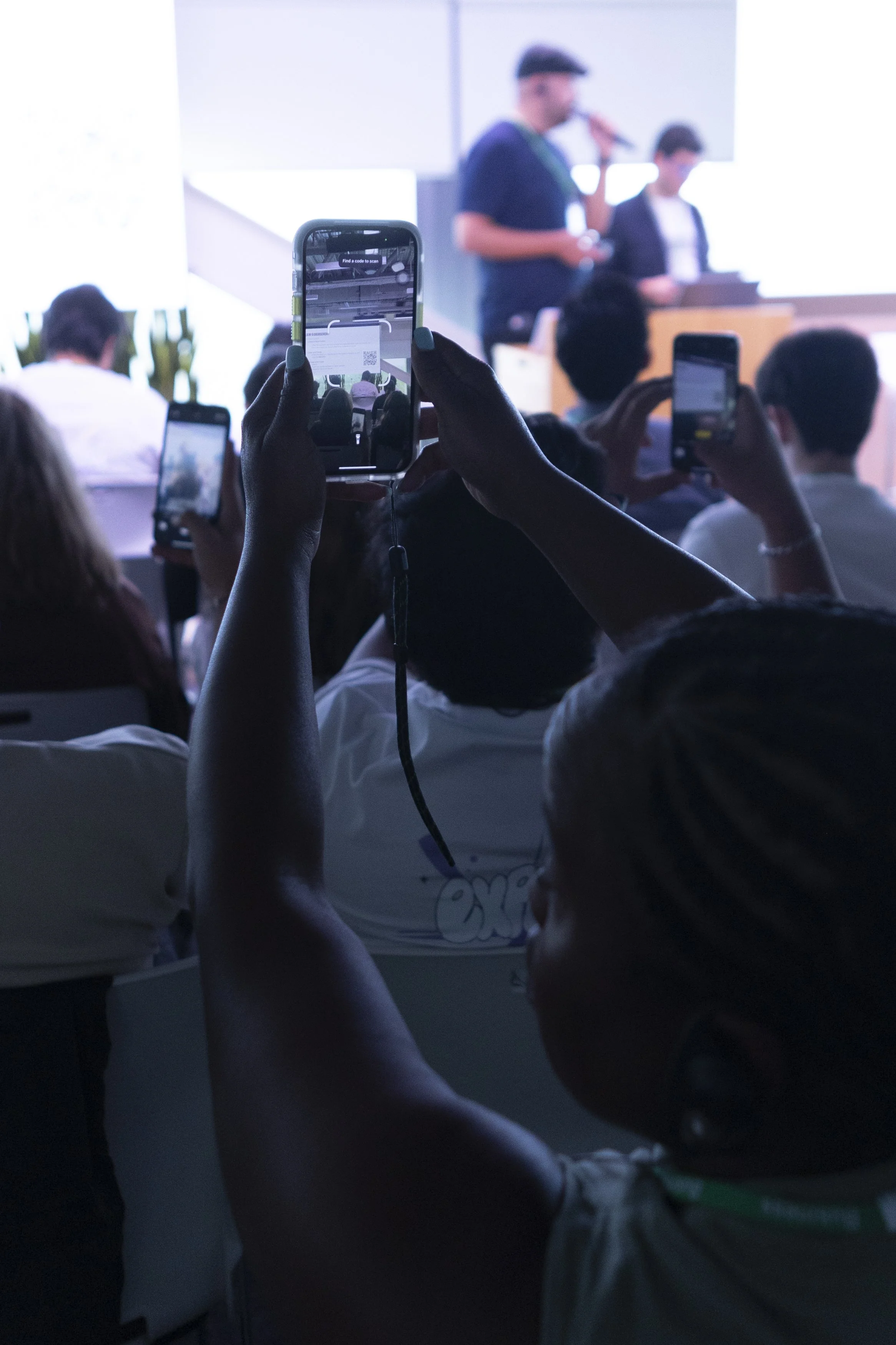 Audience at a live Mindot event holding up smartphones to photograph a speaker on stage