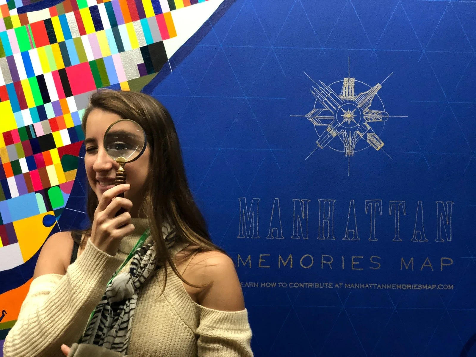 Young woman holding a magnifying glass in front of a Manhattan Memories Map display at a Mindot event