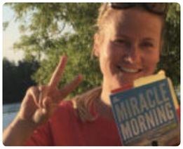Woman near water holding The Miracle Morning book