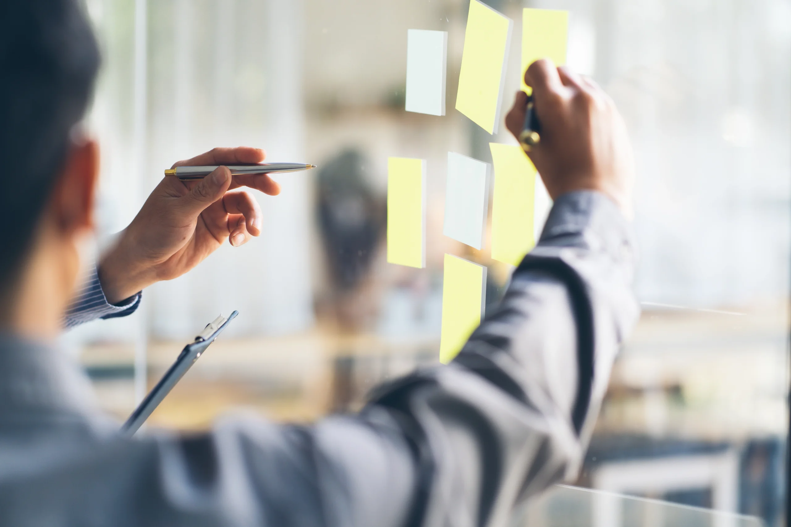 Two people placing sticky notes on a glass wall during a strategy session