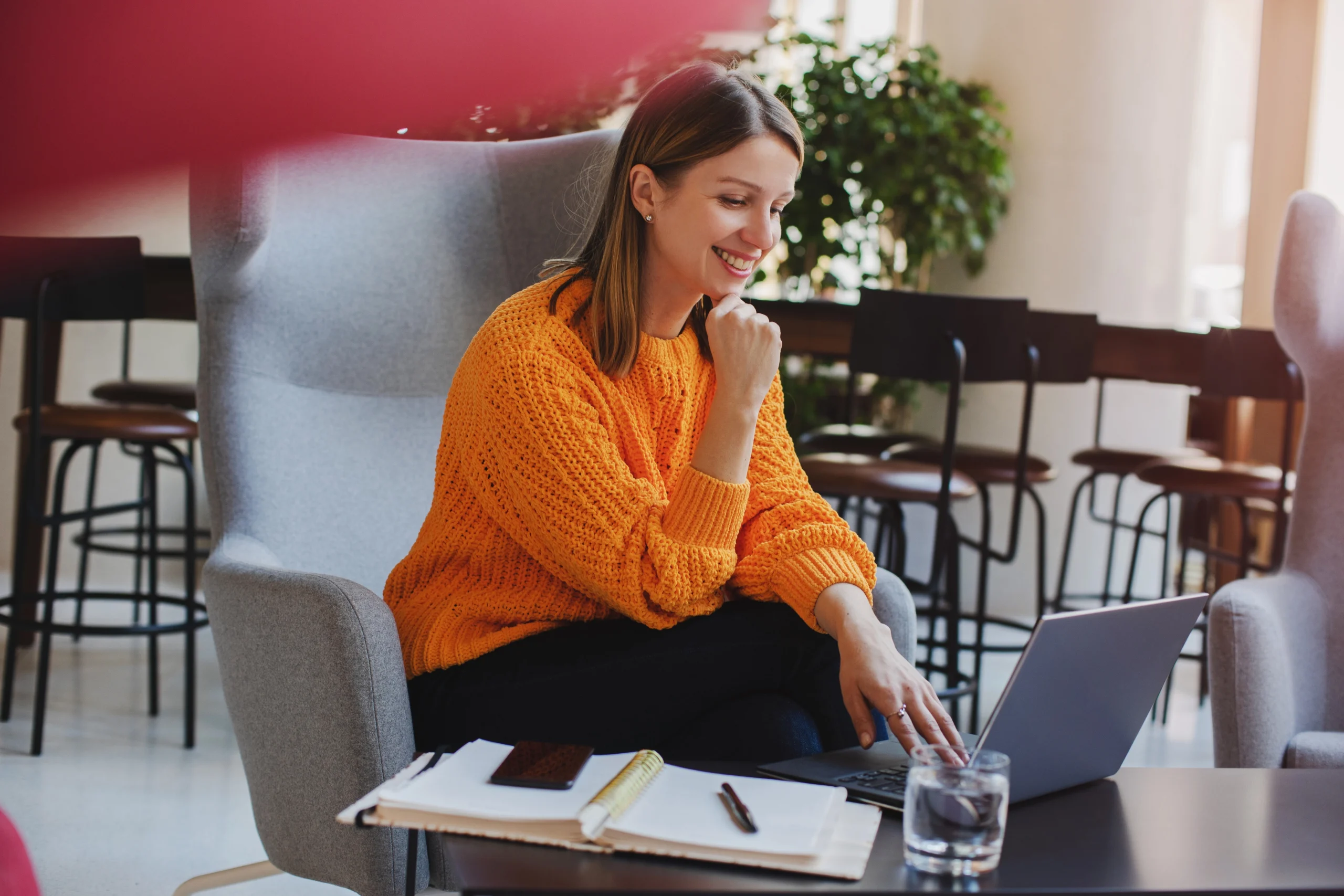 Woman in an orange sweater working on a laptop in a lounge chair