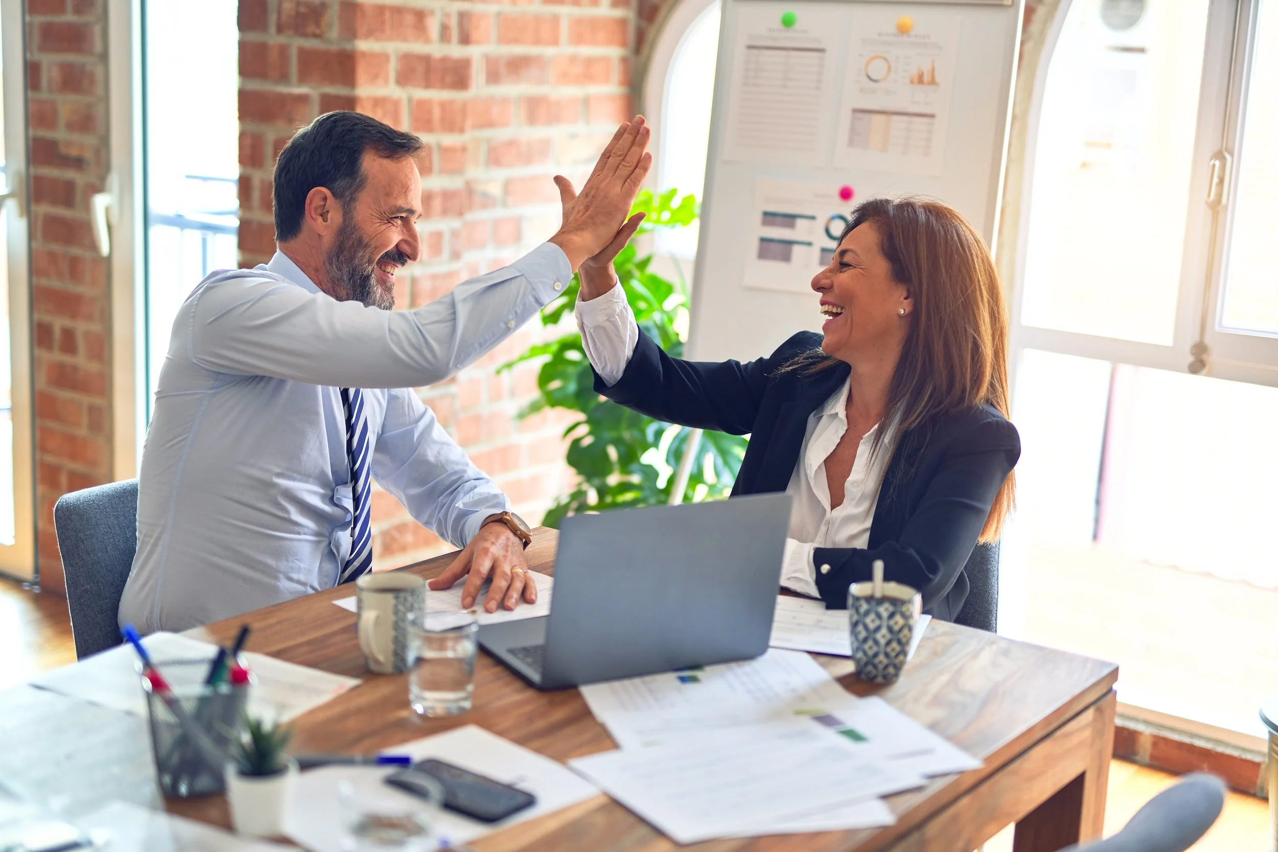 Two colleagues celebrating a win with a high five at a desk