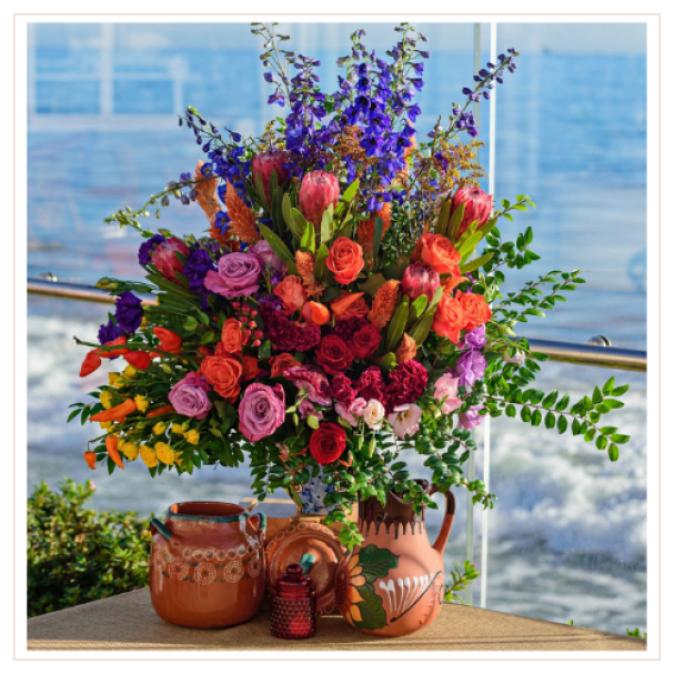Vibrant floral arrangement in a terracotta pitcher with ocean backdrop