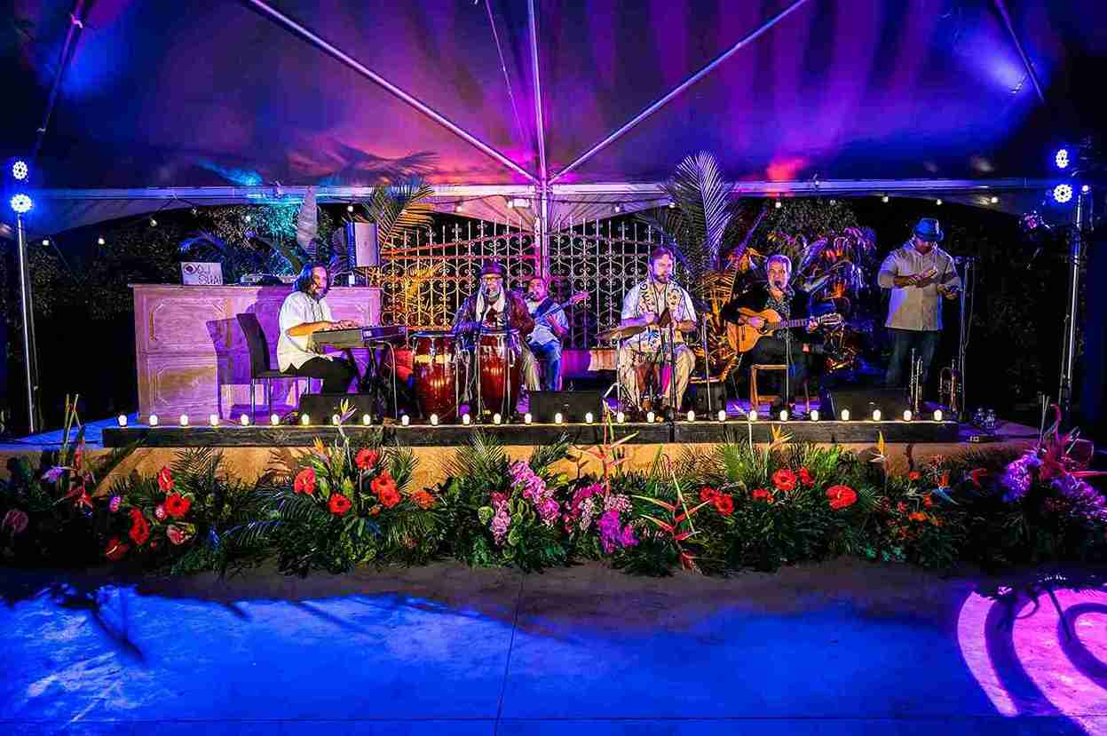 Live band performing on a tropical-decorated stage with purple uplighting
