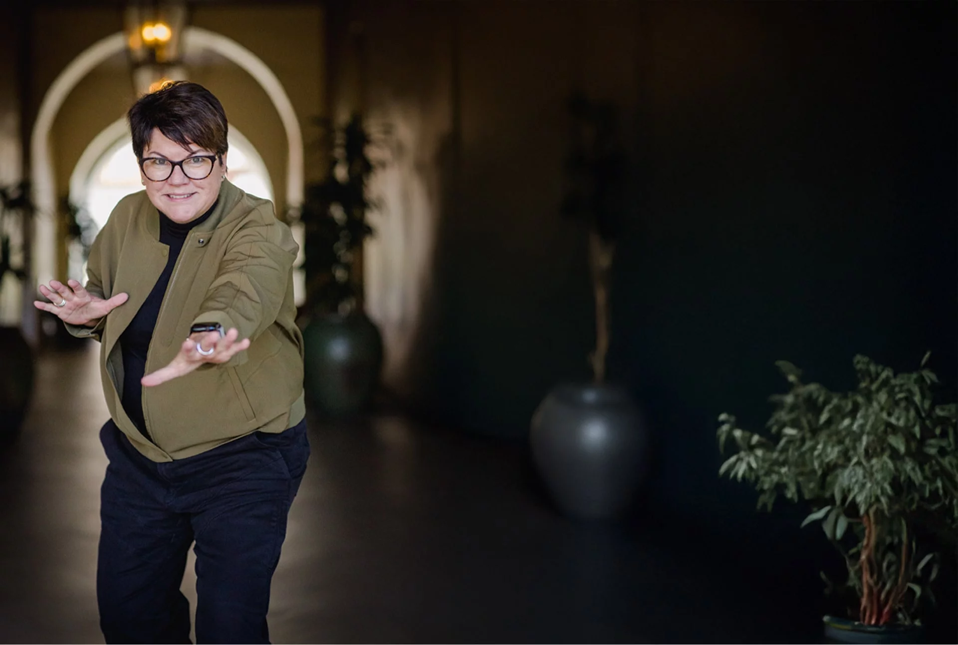 Coach Mo Faul in an olive green jacket gesturing with both hands in an arched hallway