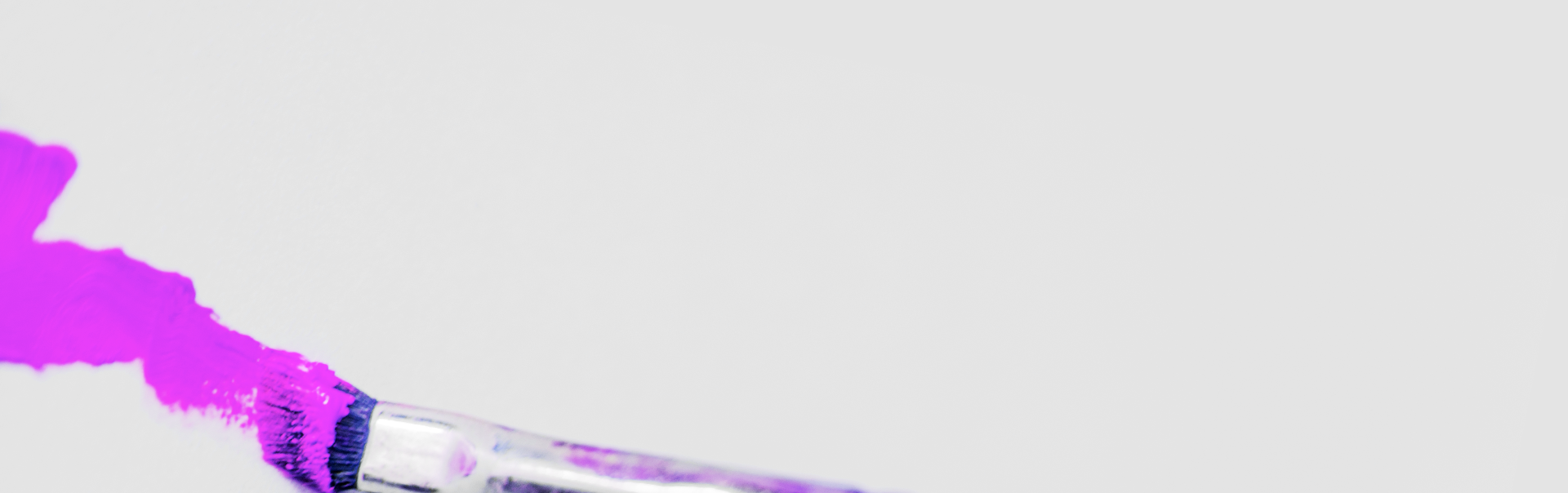 A brush laying down a bold magenta paint stroke across a light grey surface.