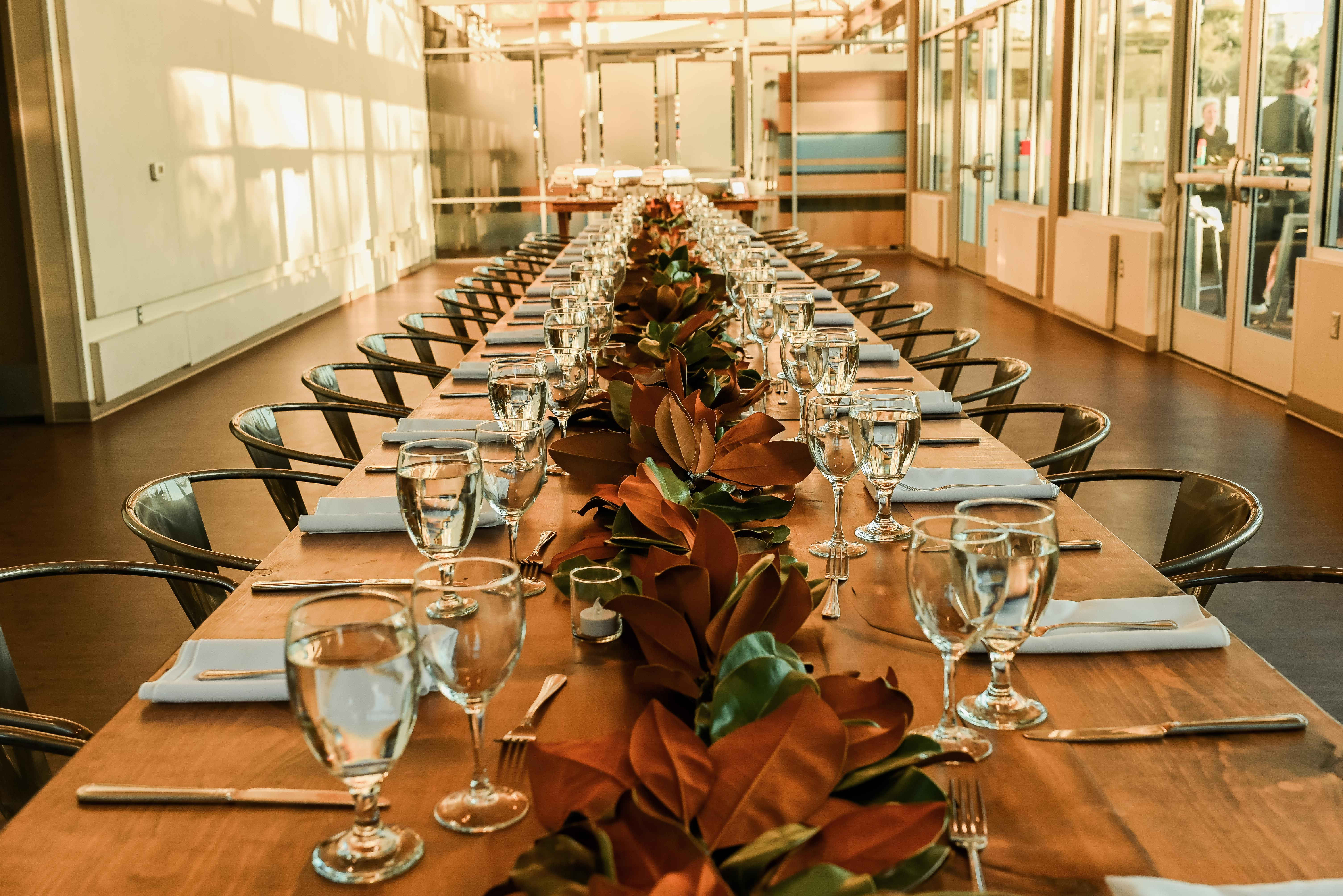 Long elegantly set banquet table with magnolia garland centerpiece in a glass-walled venue