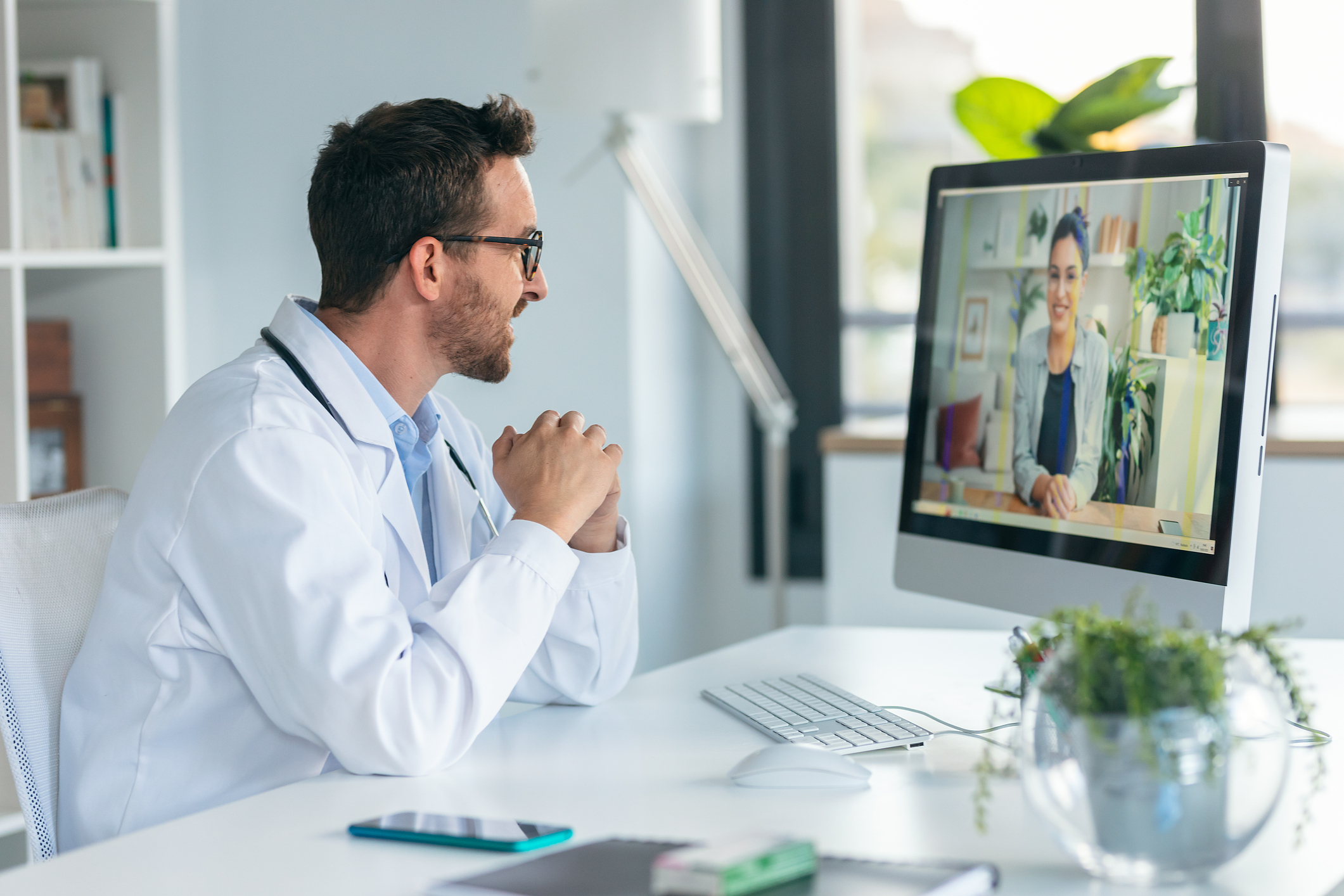 Physician in a white coat speaking with a colleague on a video call