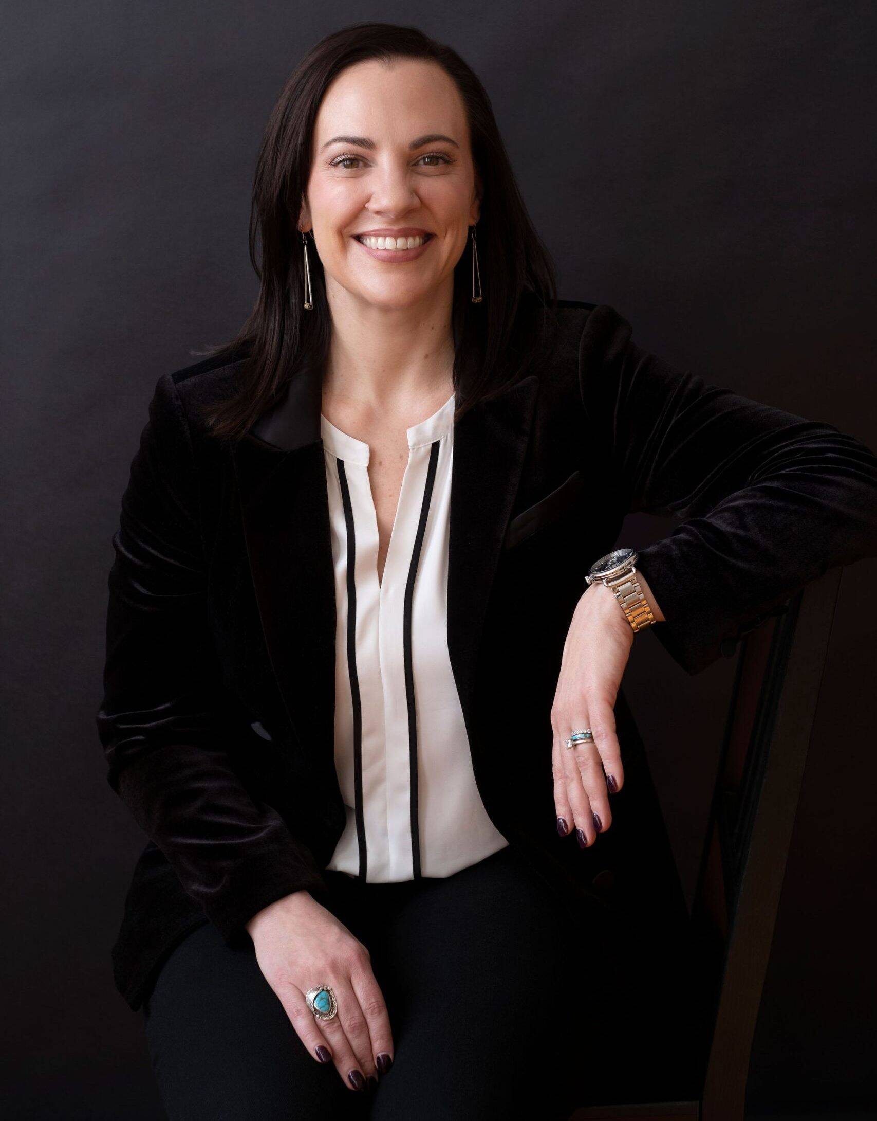 Natalie Micale seated in a black velvet blazer and white blouse, formal portrait