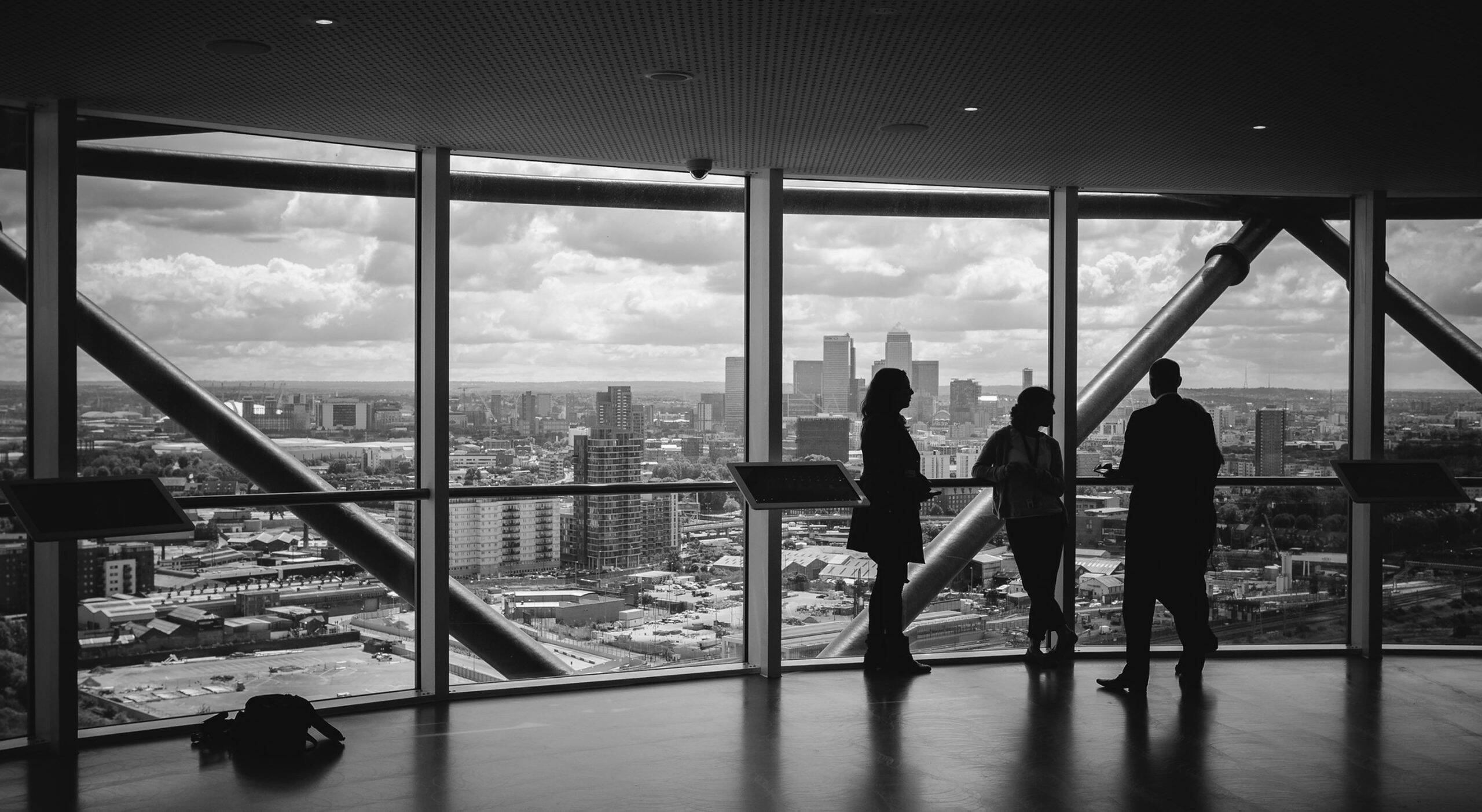 Silhouettes of three business professionals at floor-to-ceiling windows overlooking a city skyline