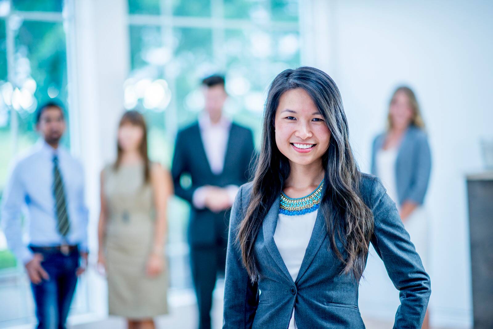 A leader in a grey blazer walking with her team through a bright office lobby