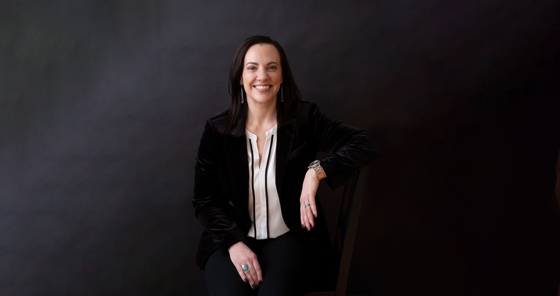 Natalie Micale, executive coach, seated in a black velvet blazer against a dark background