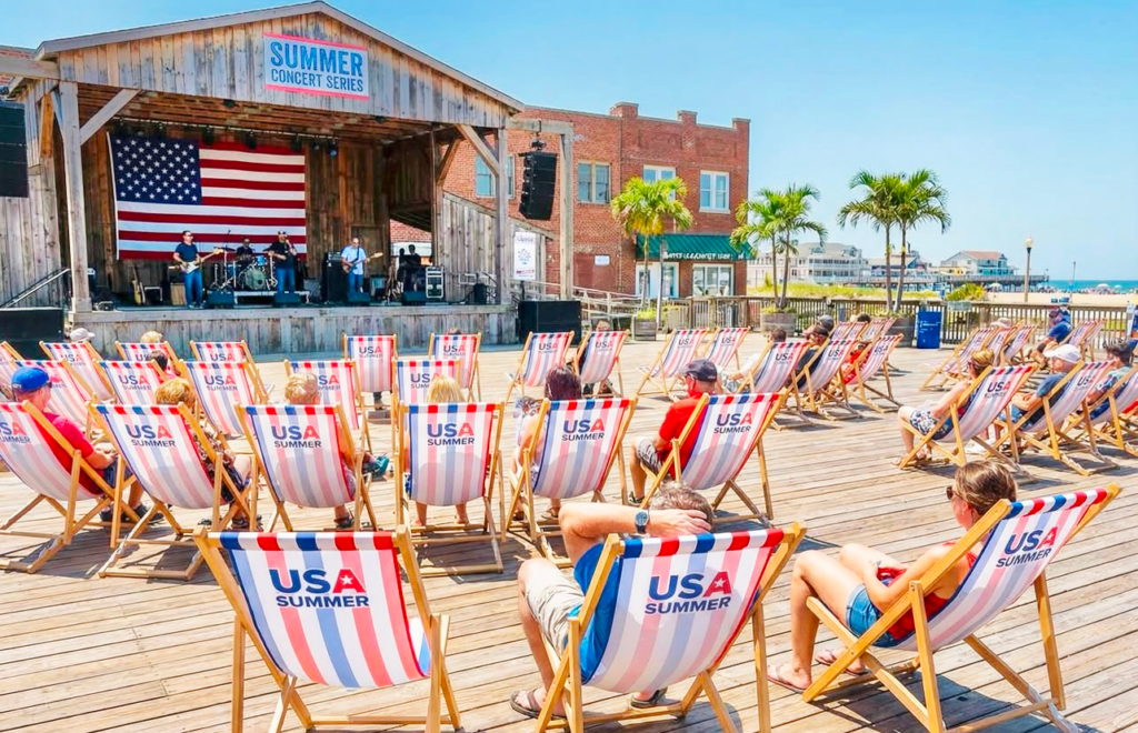 Rows of branded USA Summer wooden deckchairs on a boardwalk facing a Summer Concert Series stage