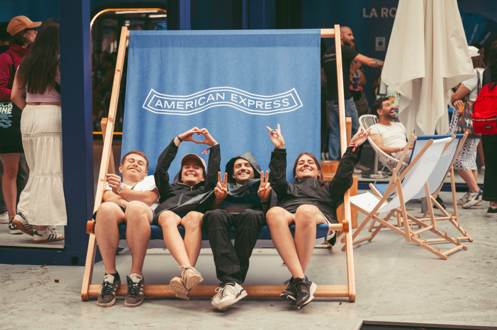 Four young people piled into an oversized American Express branded wooden deckchair